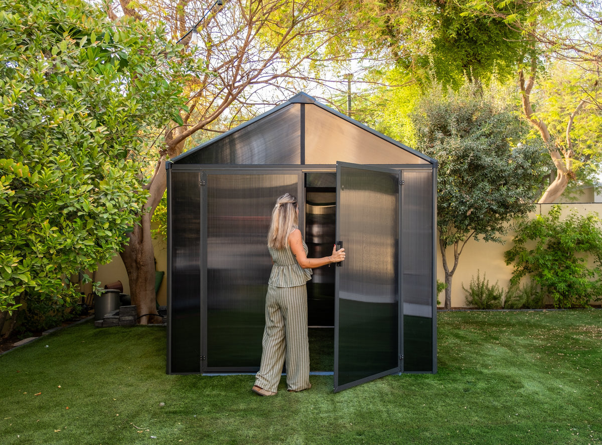 A person opening the door of a Domer Standard Slate grey shed with Black profile in a garden. #Profile colour_Black